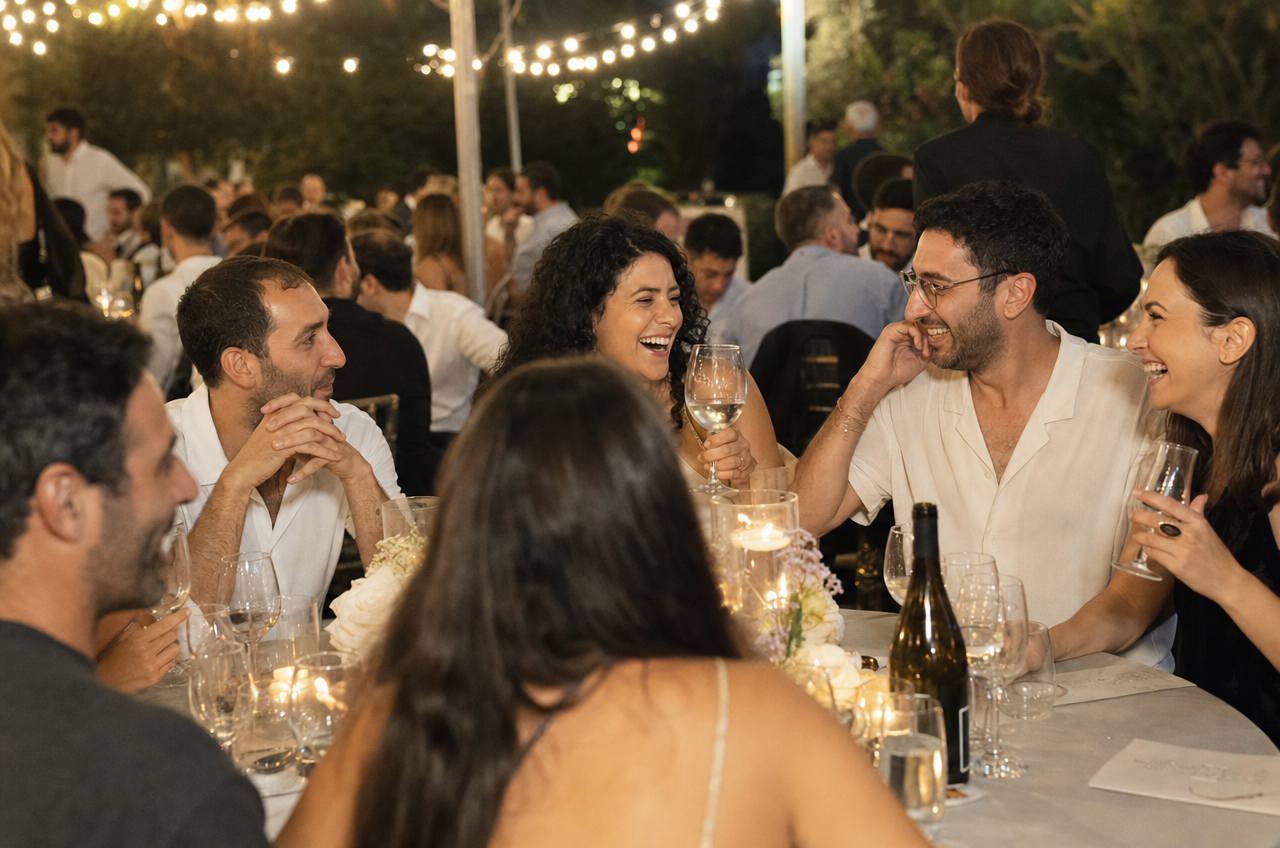 אורחים משוחחים וצוחקים סביב שולחן עגול מעוצב באירוע ערב.