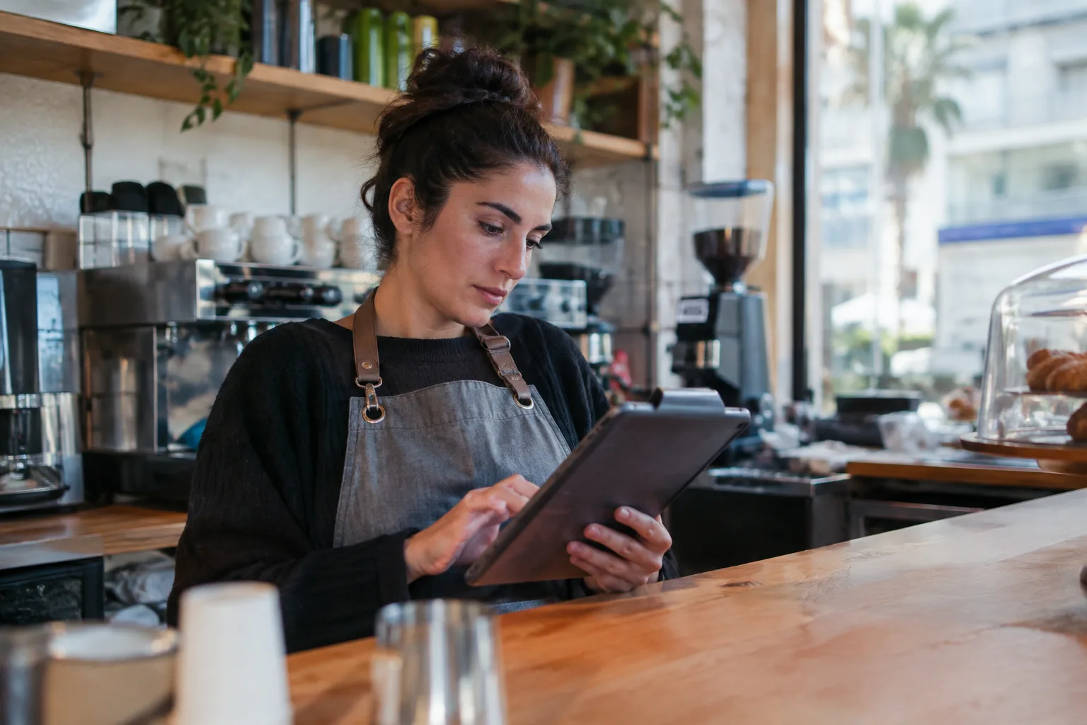 A small business owner reviews the quality of her marketing videos on a tablet in her cafe.